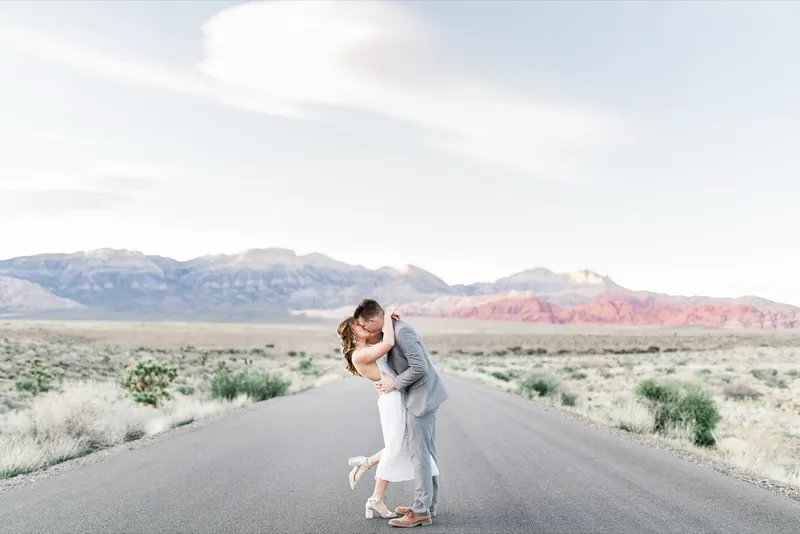A groom dipping his bride for a kiss on an empty road with the Red Rock Canyon cliffs behind them