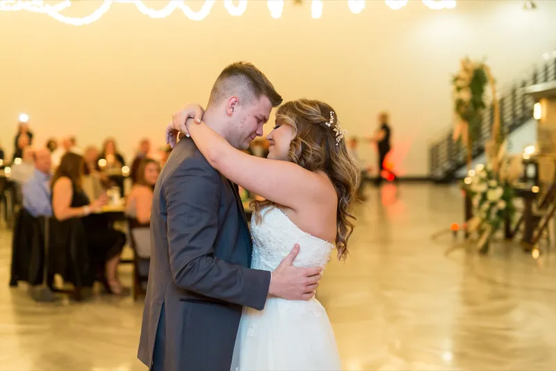 Bride and groom holding each other close during their first dance with guests watching from the tables behind them