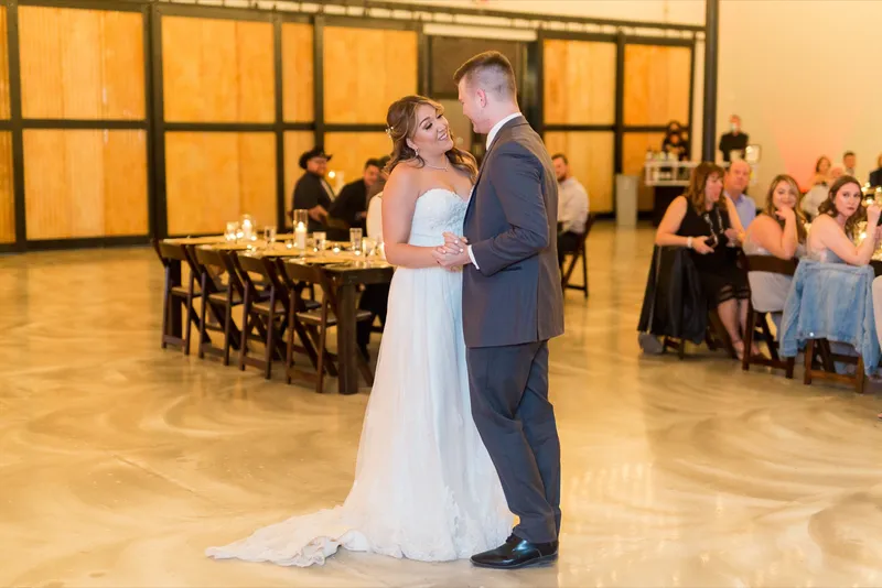 The couple dancing alone in the middle of the open floor with the wood wall and the candlelit tables behind them