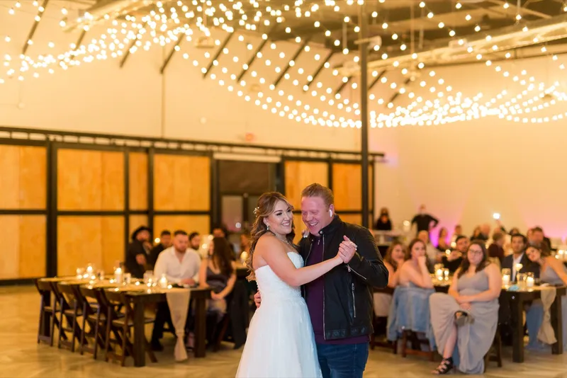Bride dancing with a guest under the string lights while the rest of the room watches from the tables