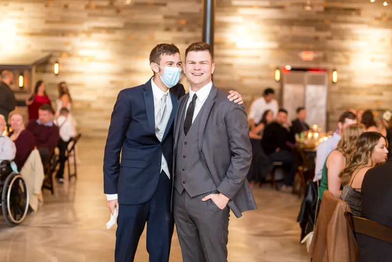 Two guests in suits standing with an arm around each other on the dance floor while others sit at the tables