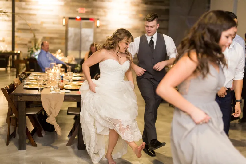 Bride gathering up her skirt to dance barefoot with her guests on the concrete floor