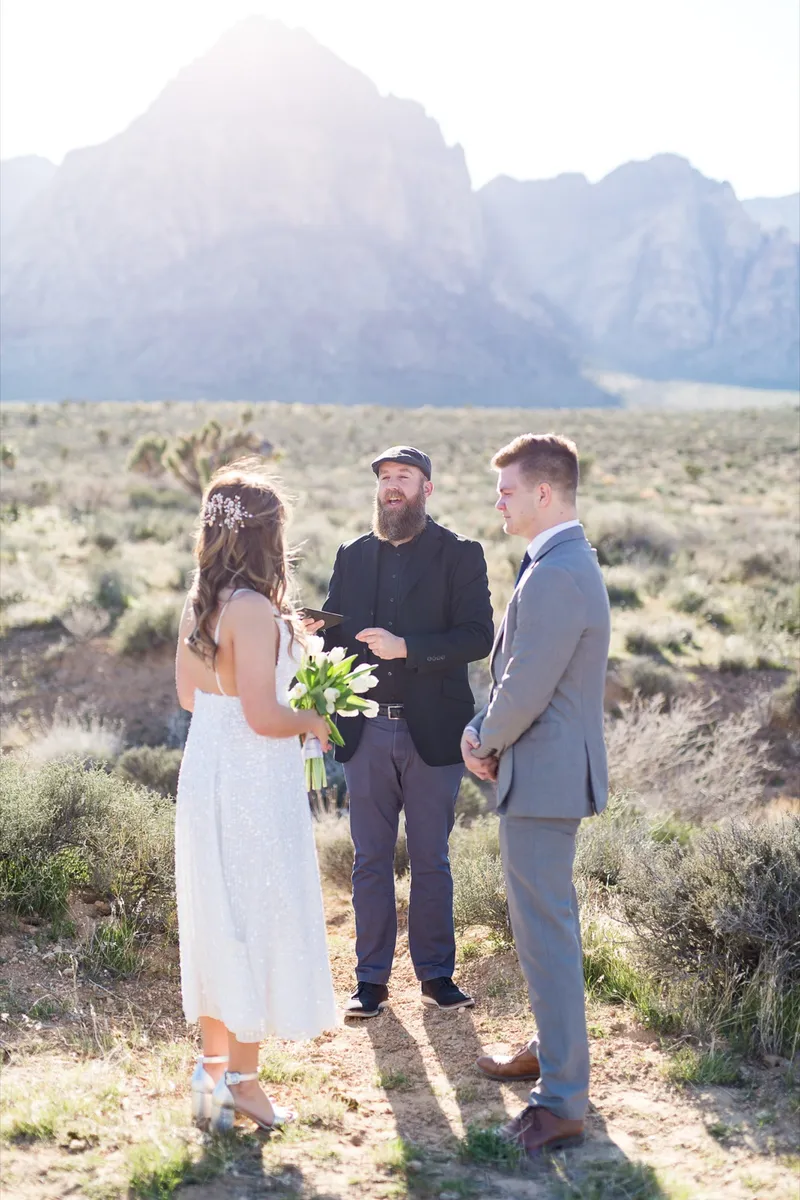 Bride holding white tulips as she faces her groom during the ceremony, officiant beside them