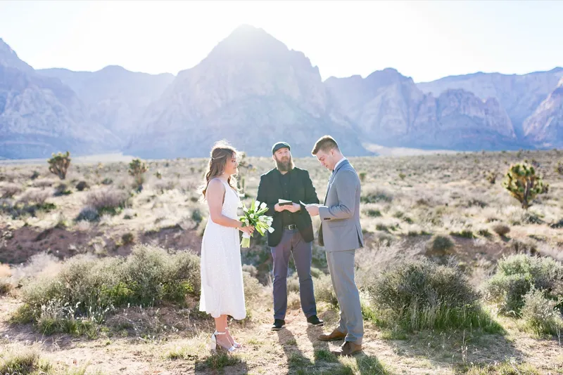 Couple facing each other with their officiant reading between them and the mountains behind