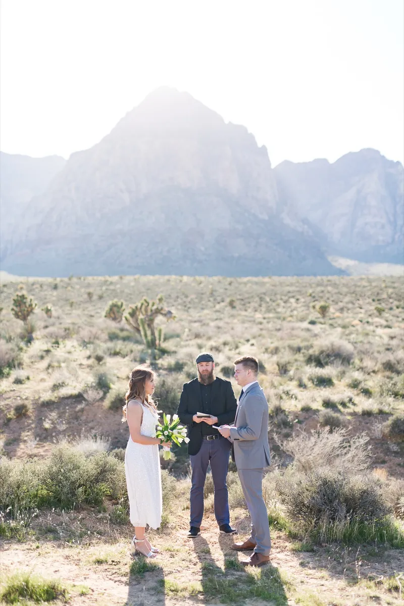 The whole ceremony seen from far back, three people alone under the mountain ridge