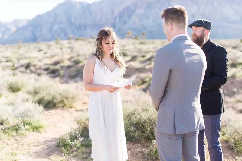 Bride reading her vows from a folded page with her groom listening in front of her