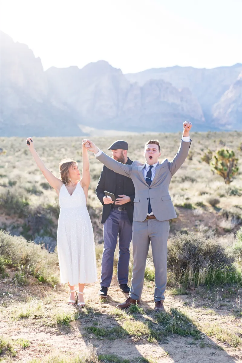 Bride, groom and officiant throwing their arms up in celebration after the ceremony