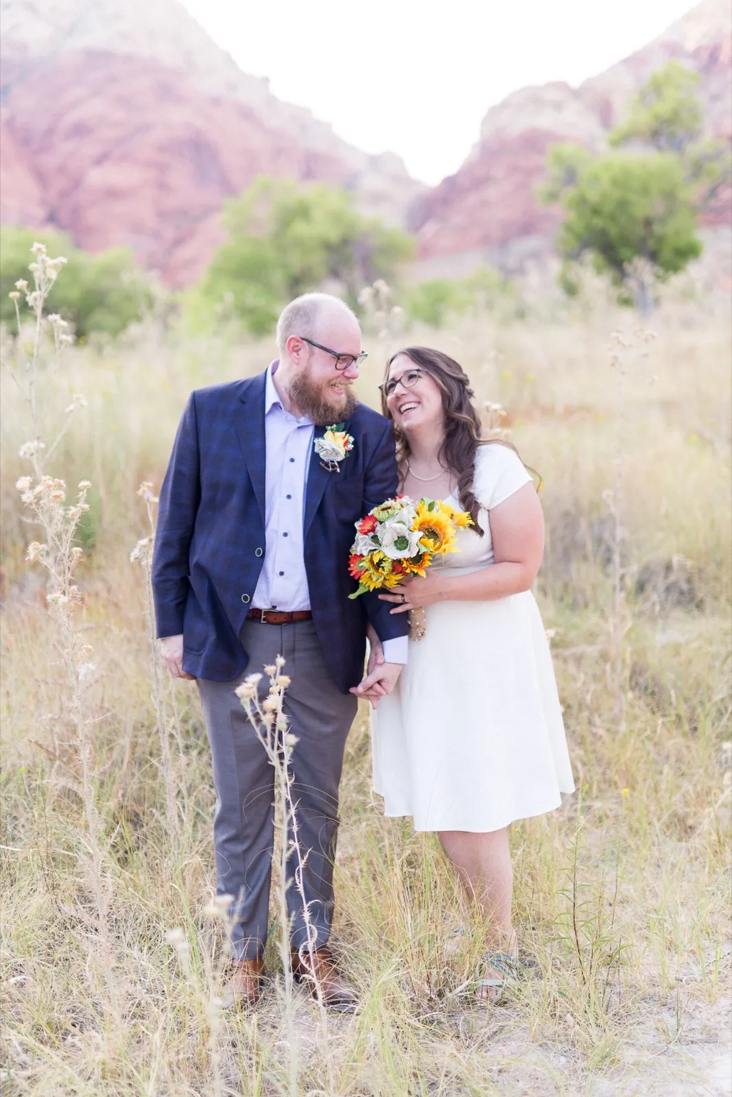 Bride laughing with a sunflower bouquet beside her groom in the tall grass at Red Rock Canyon