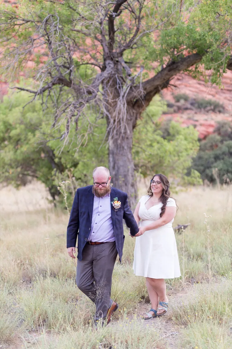 Bride and groom walking through the grass together, both laughing