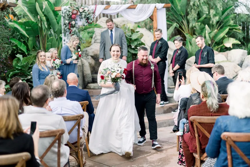 Couple walking out of the ceremony hand in hand past the seated guests, the bride laughing