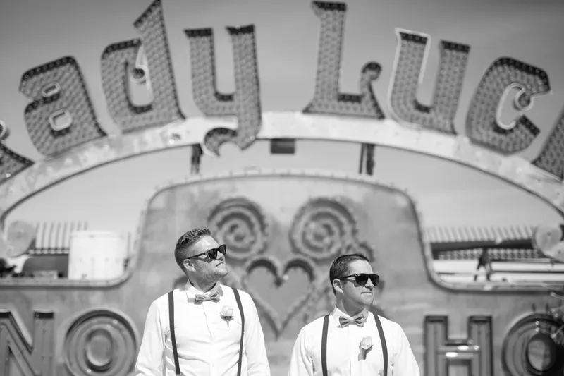 Black and white frame of the groom and a groomsman in sunglasses and bow ties under a sign