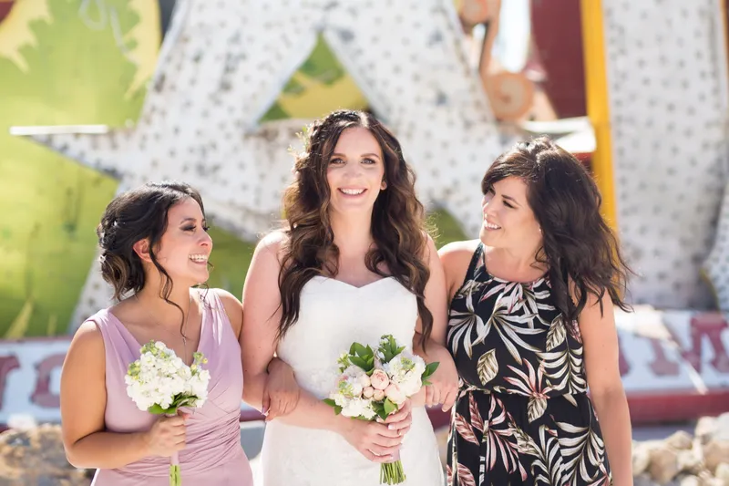 Bride standing with two women in front of the neon, all holding small bouquets