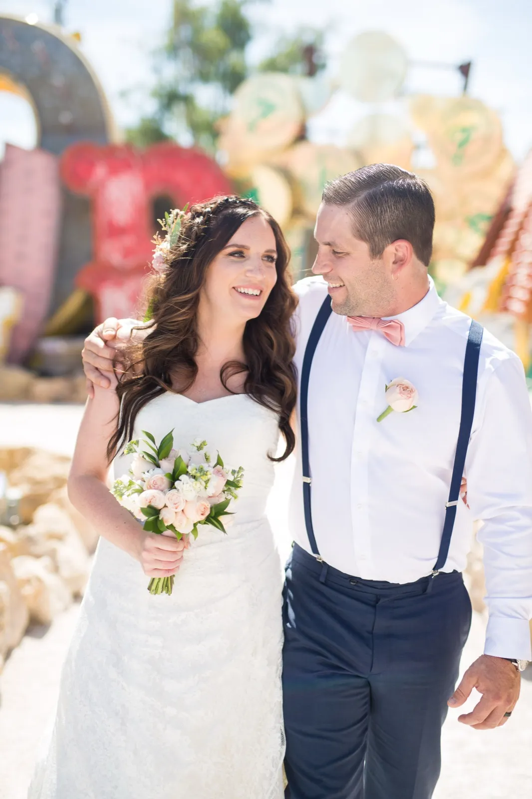 Bride in a flower crown and groom in a peach bow tie smiling close together among the old signs