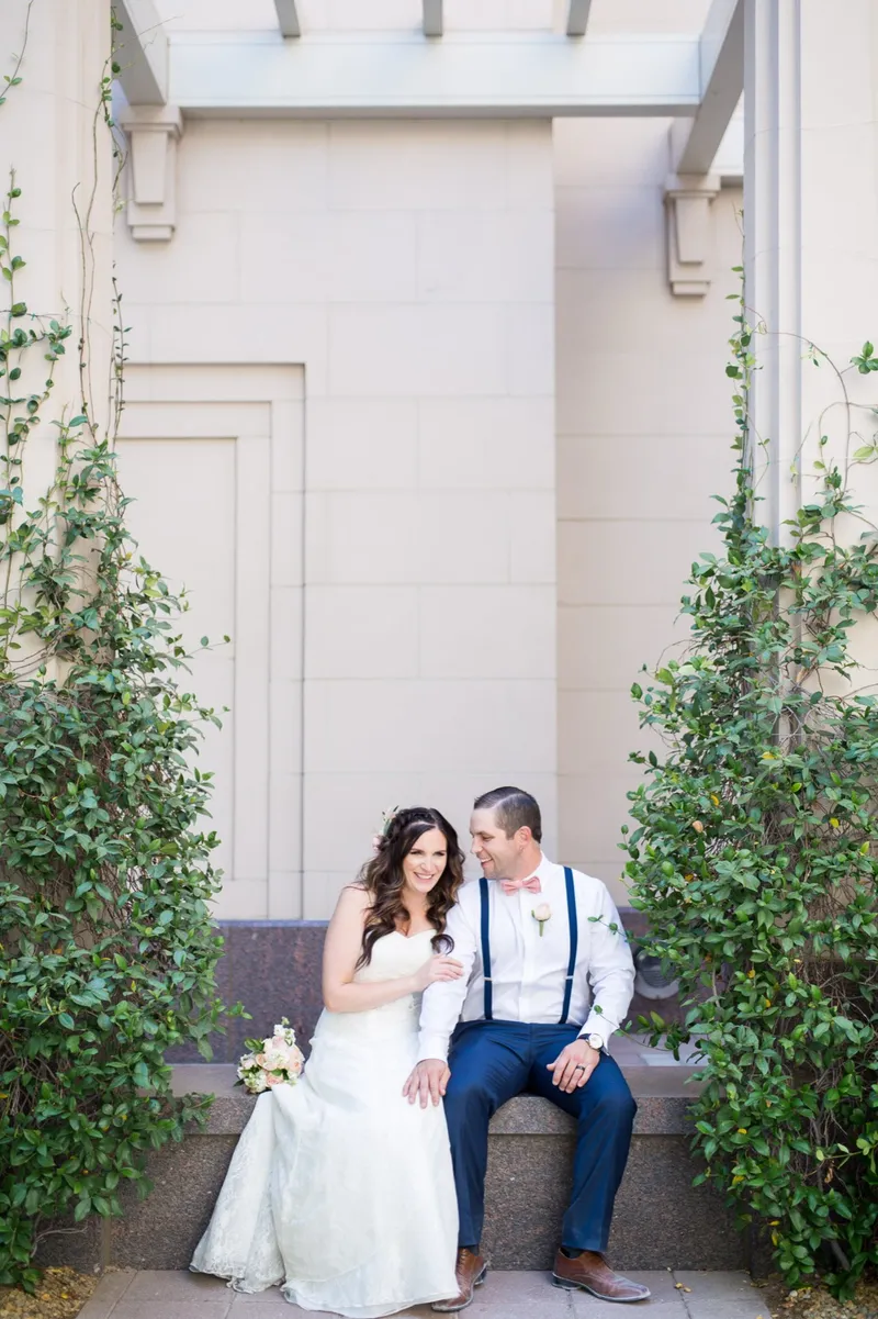 Couple sitting on a stone ledge under a pergola, climbing vines running up the wall on both sides of a tall window behind them