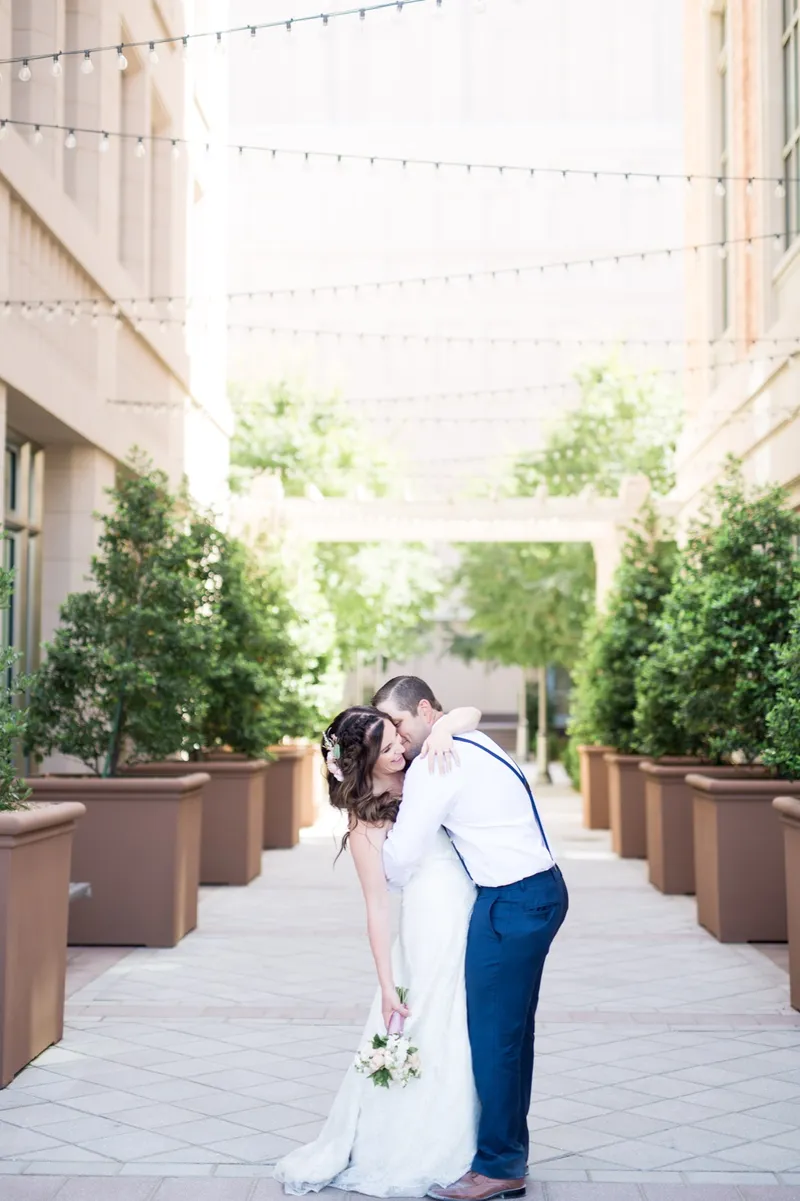 Groom dipping his bride for a kiss on the walkway with the string lights and stone buildings rising on both sides