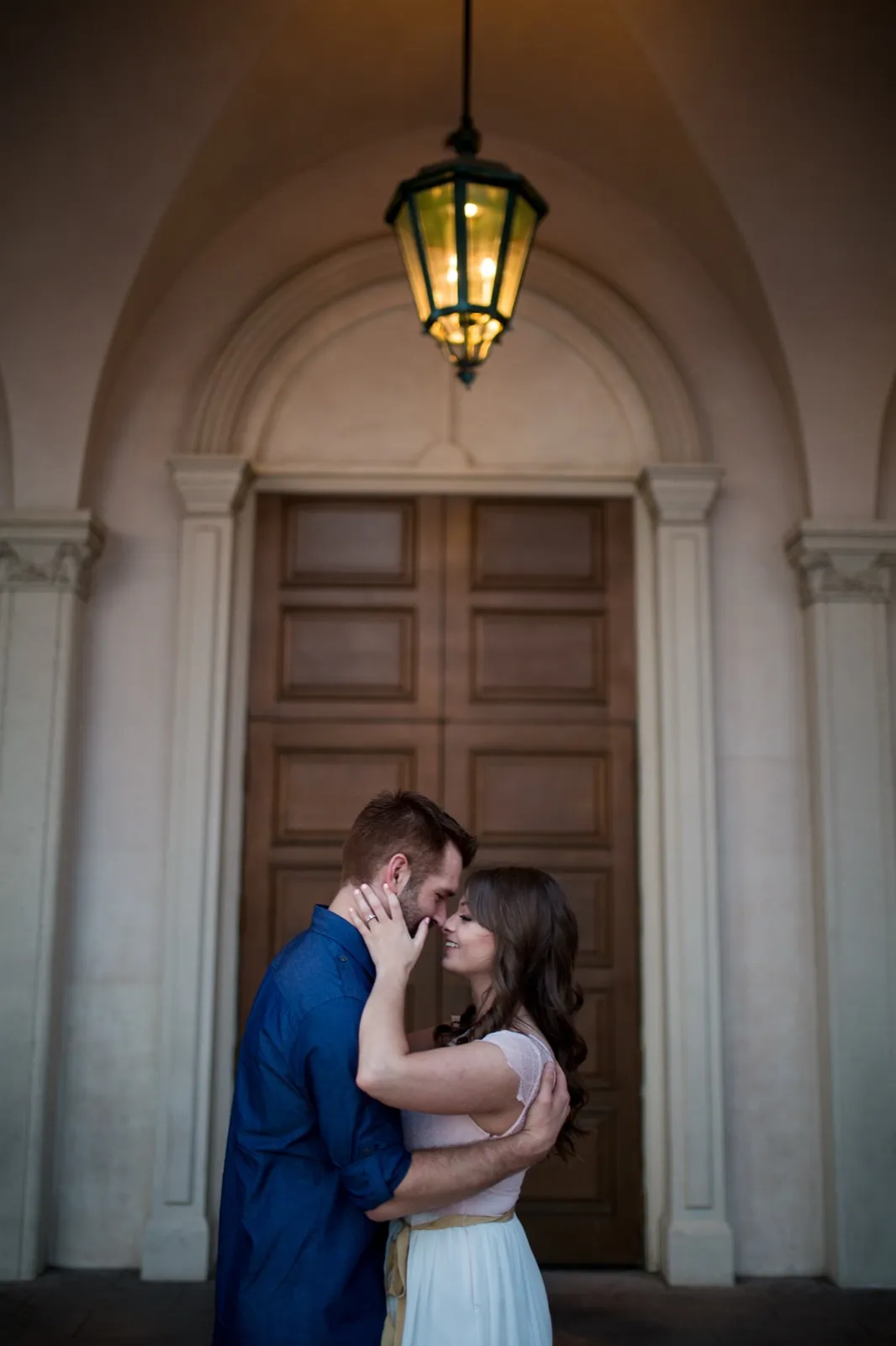 Couple about to kiss under a lit hanging lantern in front of tall wooden double doors