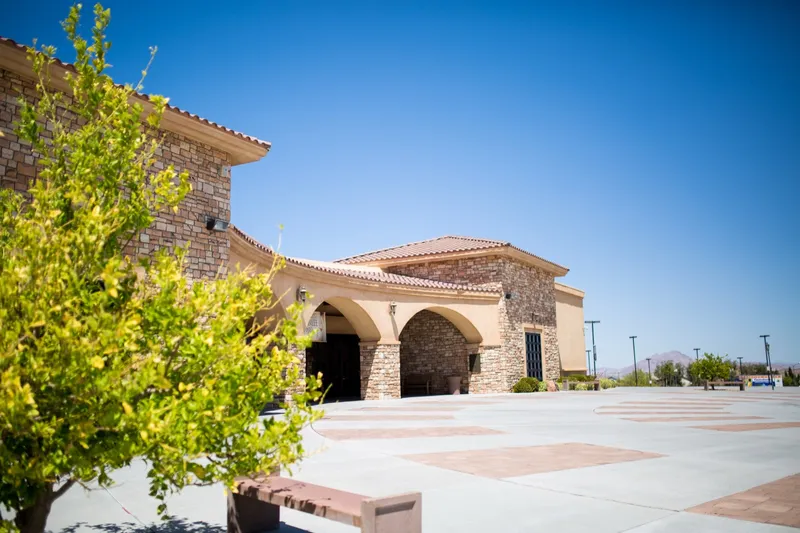 The stone and stucco church with its red tile roof and arched entry, seen across the empty paved plaza on a clear day