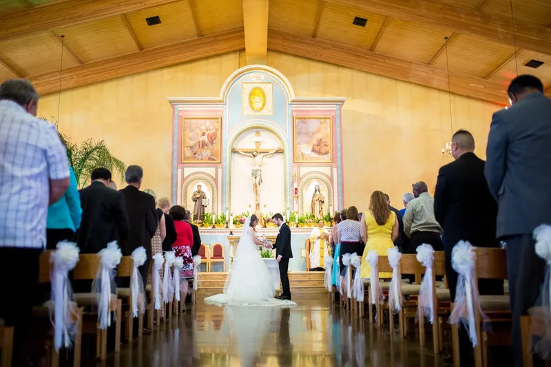 Wide view up the aisle during the ceremony, the couple standing before the painted altar wall under the open wood ceiling