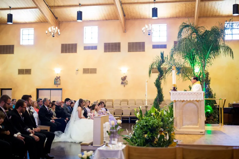The couple facing each other at the altar as the priest stands between them in white and gold vestments