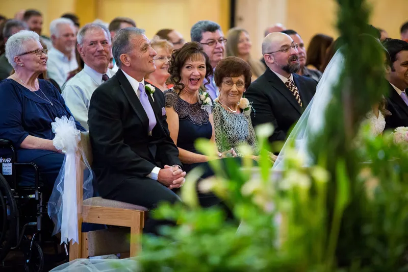 Guests watching the ceremony from their seats, some of them smiling, tall greenery in the foreground