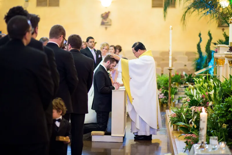 The priest laying a blessing on the groom as he kneels at the altar step