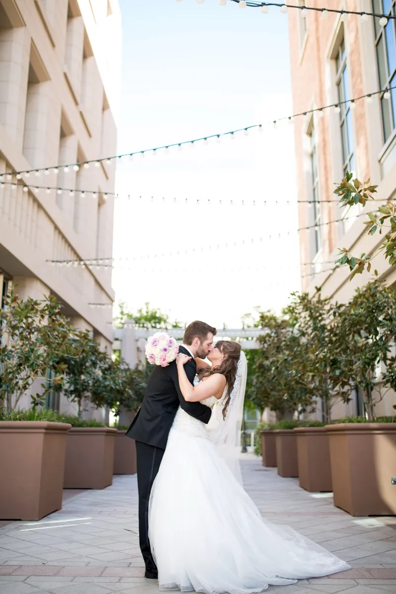 Couple kissing under the lights with her pink and white bouquet held down at her side