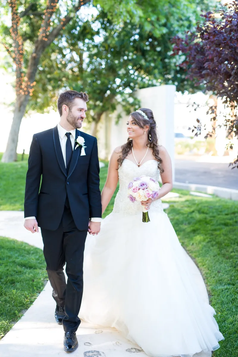 Couple walking a garden path together, the bride holding a lavender and white rose bouquet