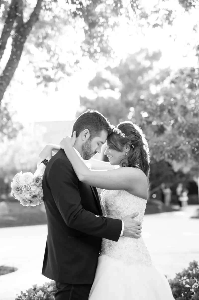 Black and white of the couple embracing with their eyes closed under the garden trees