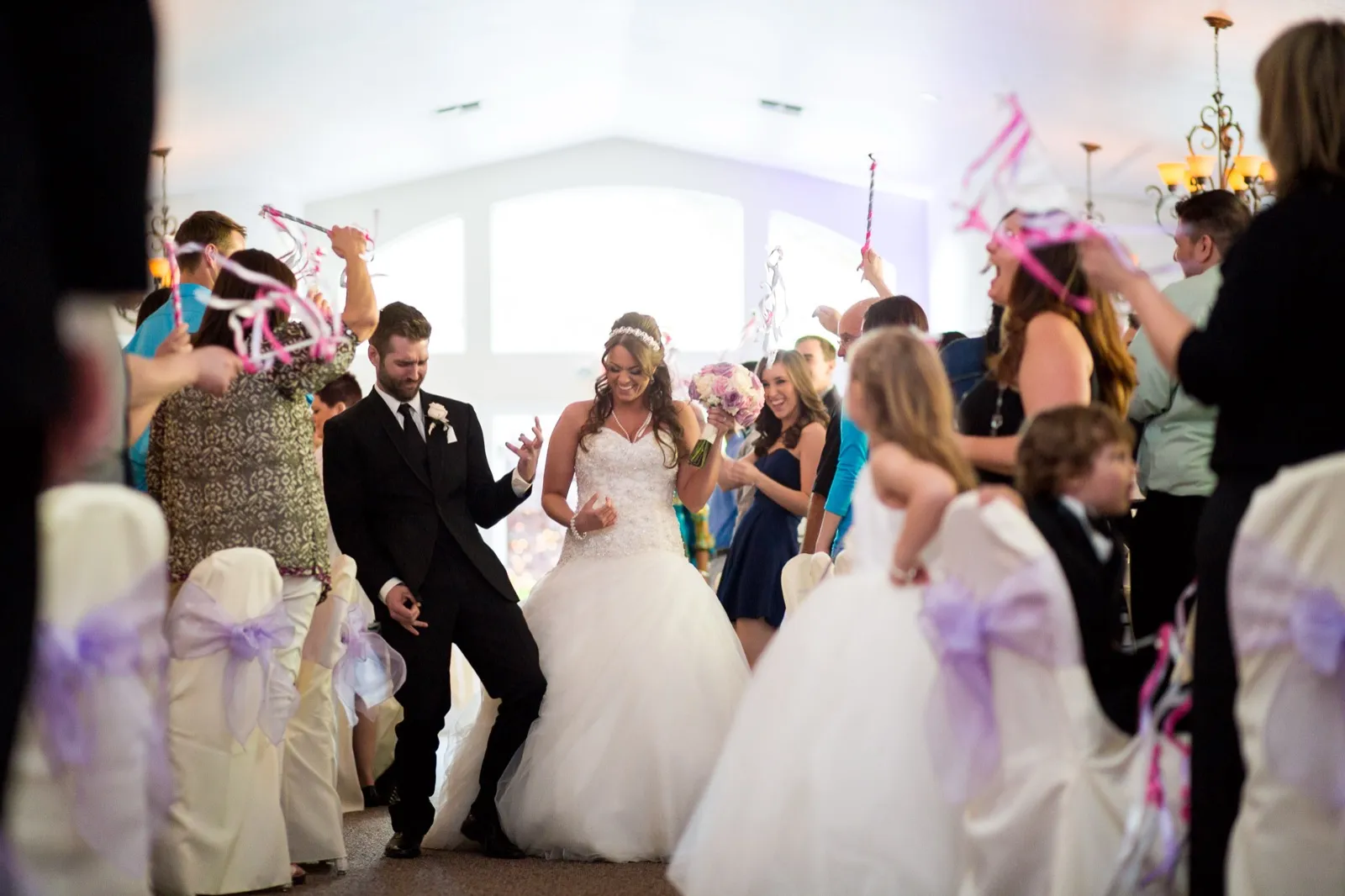 Guests wave pink and white ribbon wands as a bride and groom walk into their reception