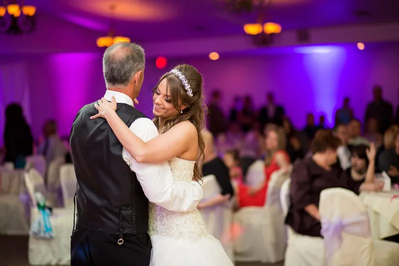 Bride dancing with a parent in the purple lit room, the two of them laughing at each other