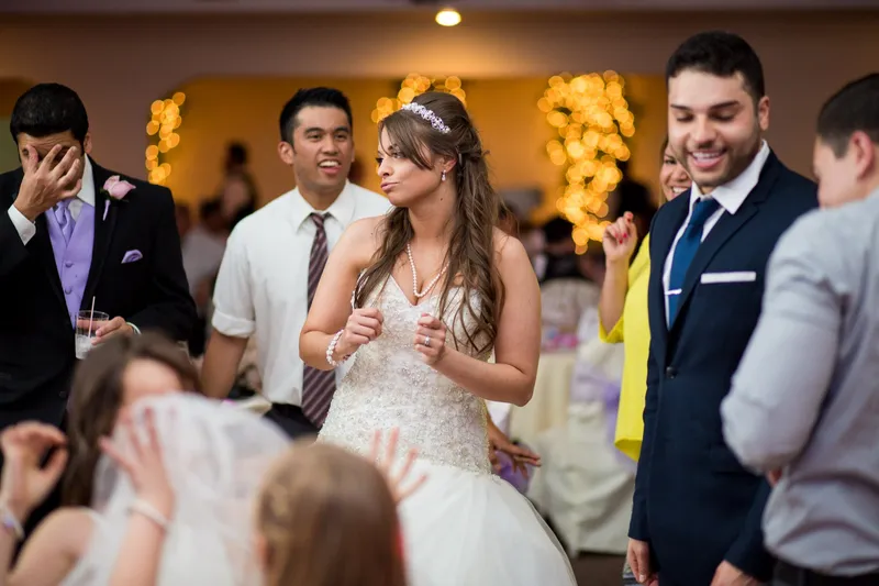 Bride dancing in the middle of a ring of guests with a photographer's light flaring behind her