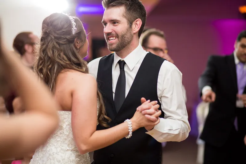 Couple dancing late in the night, the groom down to his vest and shirtsleeves, purple light behind them