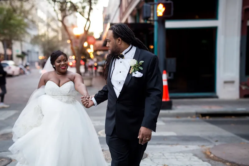 Bride and groom walking hand in hand through a downtown street at sunset