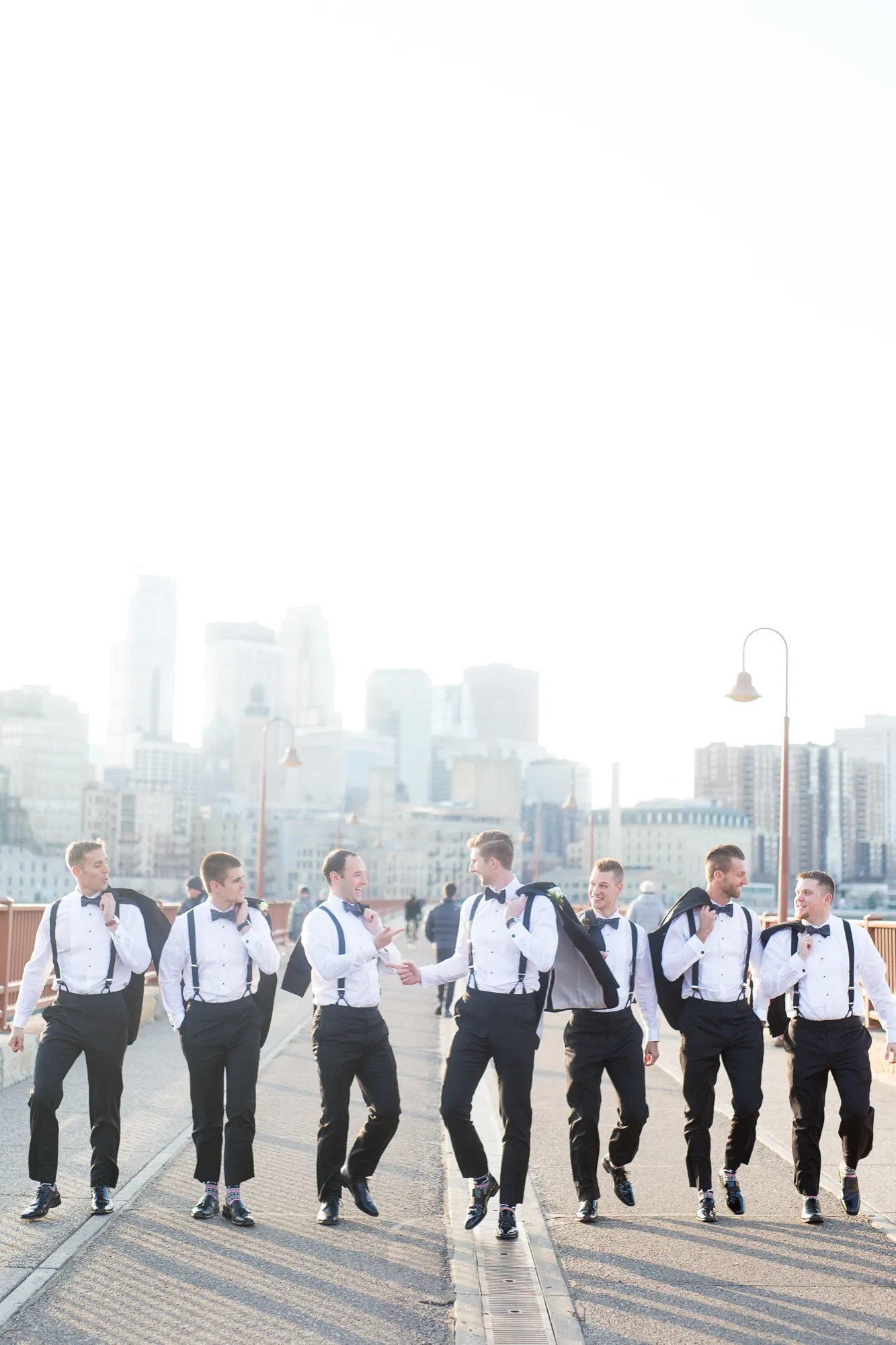 Groomsmen laughing and walking across a bridge with their jackets slung over their shoulders