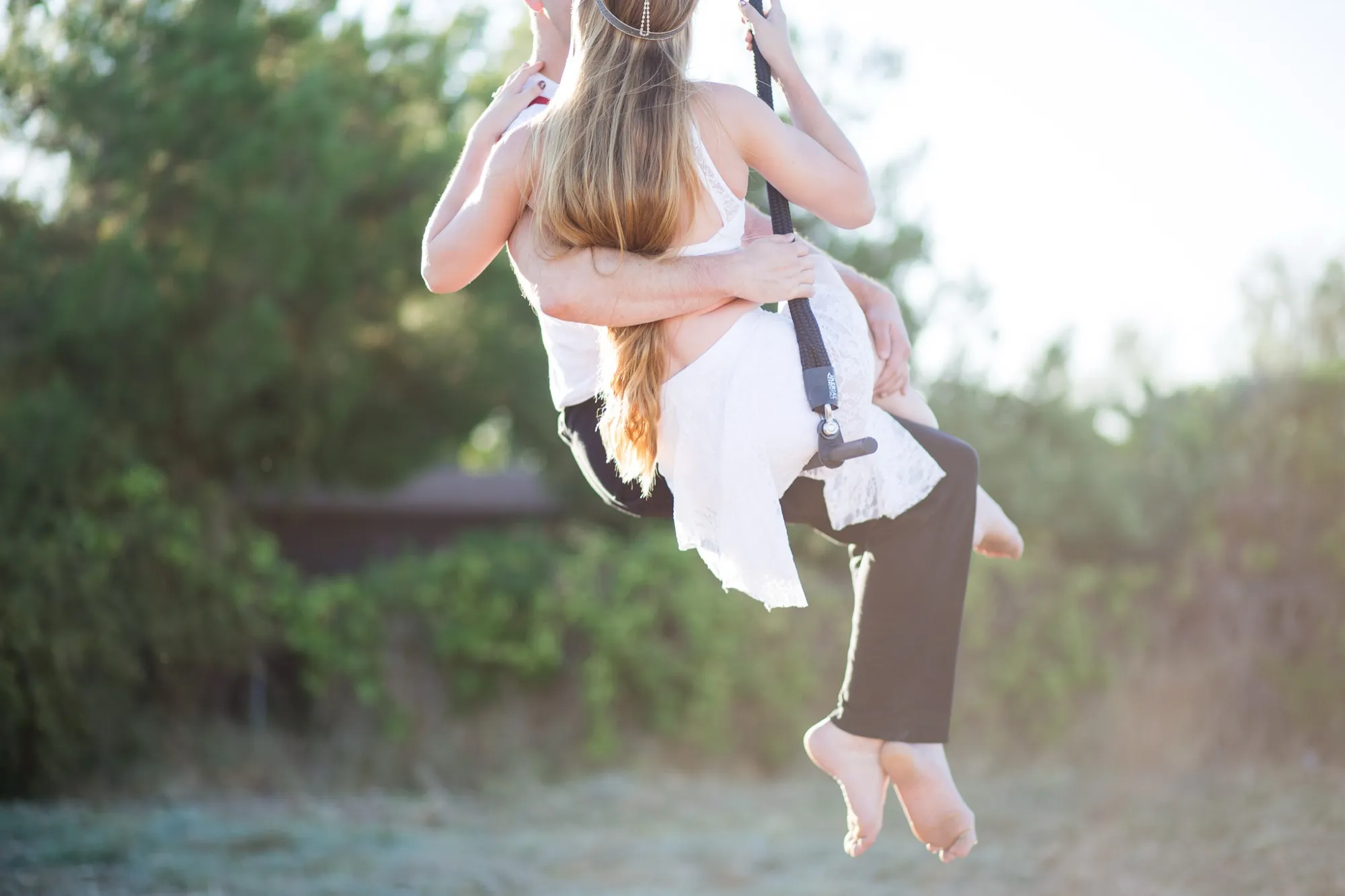 An engaged couple swinging together on a rope swing in golden evening light