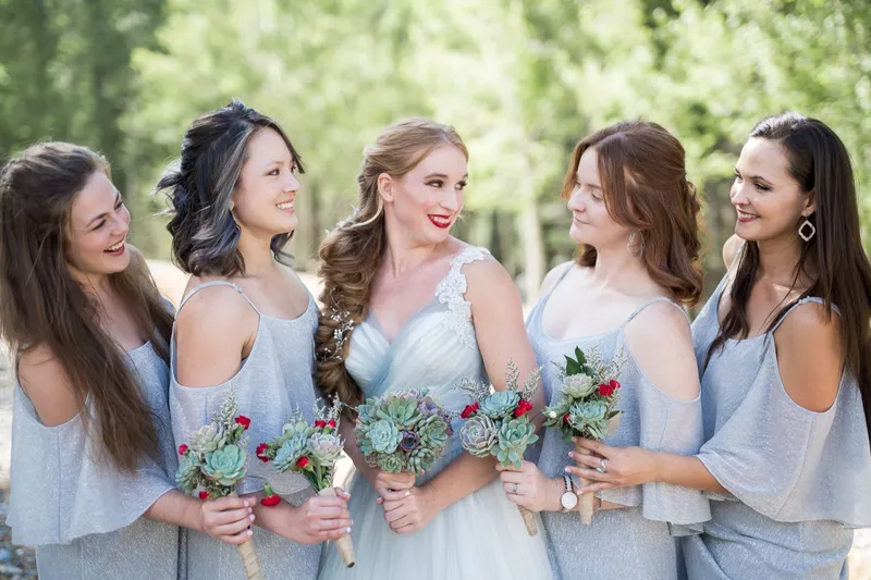 Bride laughing with two of her bridesmaids in dusty blue gowns holding succulent bouquets