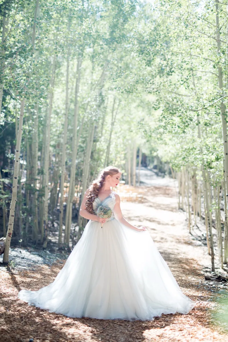 Bride in a full ballgown standing among the tall aspen trunks