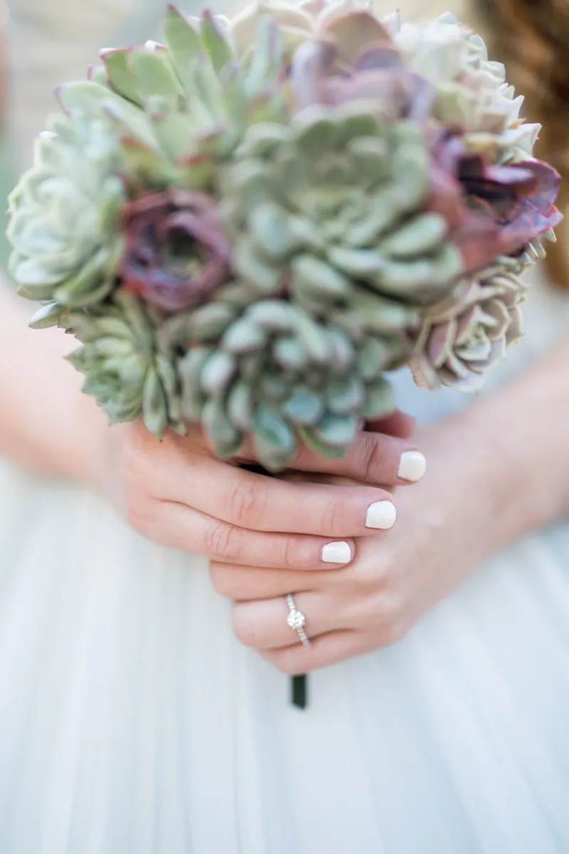 Close view of a succulent bouquet held in both hands with a wedding band showing