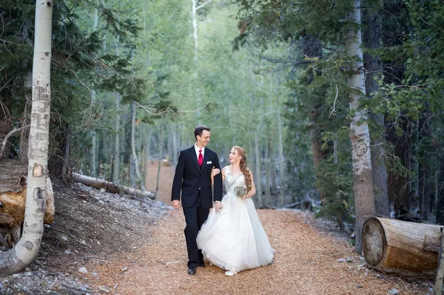 Bride and groom walking a trail through the aspens and pines on Mount Charleston, looking at each other while she carries her bouquet