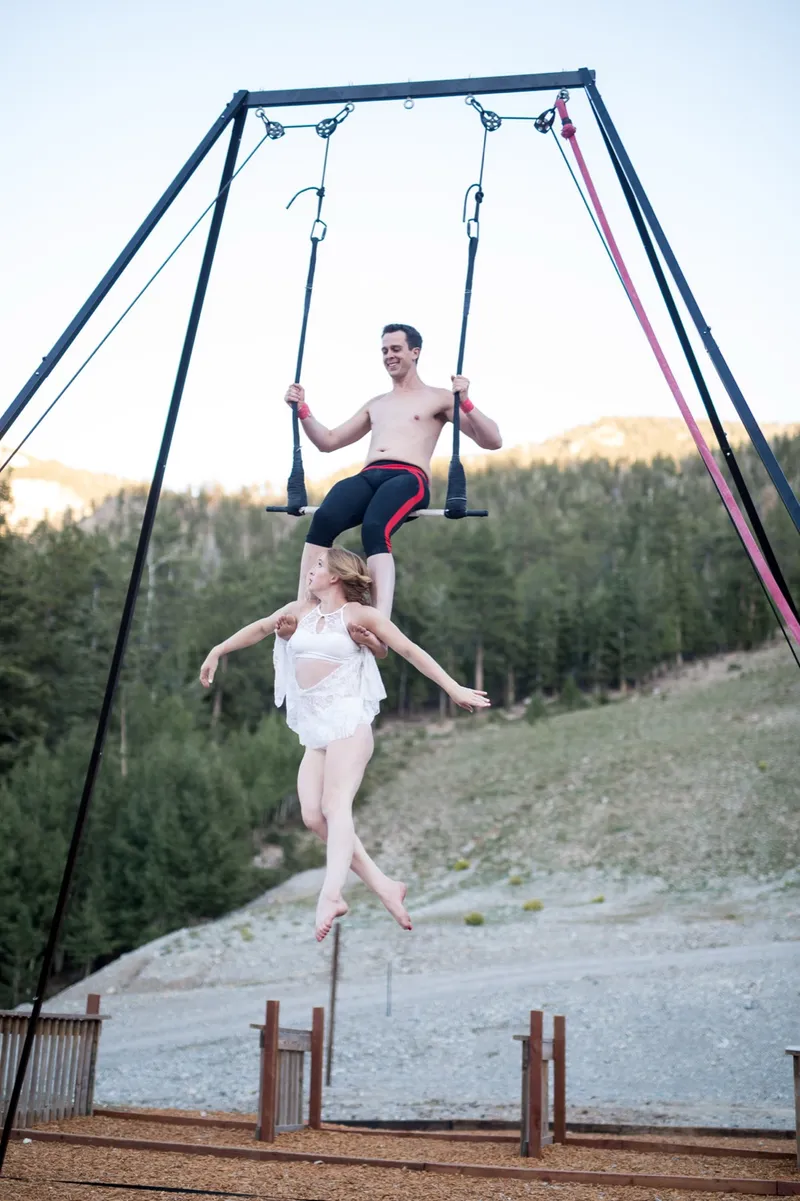 Two aerial acrobats performing on a trapeze rig above the mountain lawn