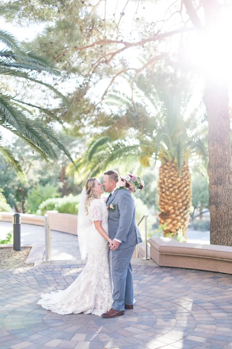 The couple kissing on the paved walkway with sun coming through the palms behind them and the bride's lace train spread across the pavers