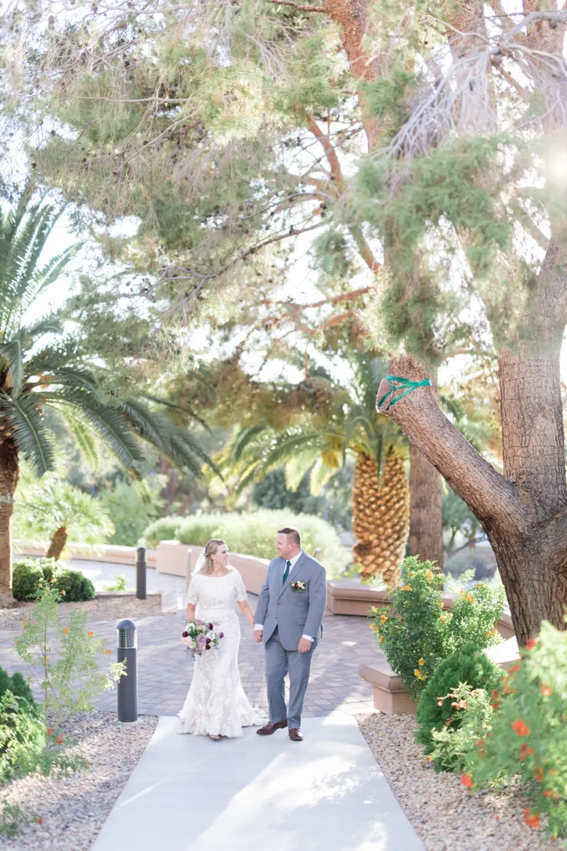 The couple standing together on the concrete path with date palms and low flowering shrubs down both sides