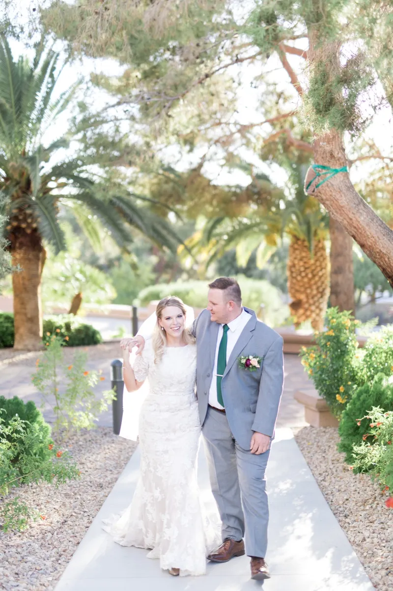 The couple walking toward the camera laughing, the groom in a grey suit and a green tie