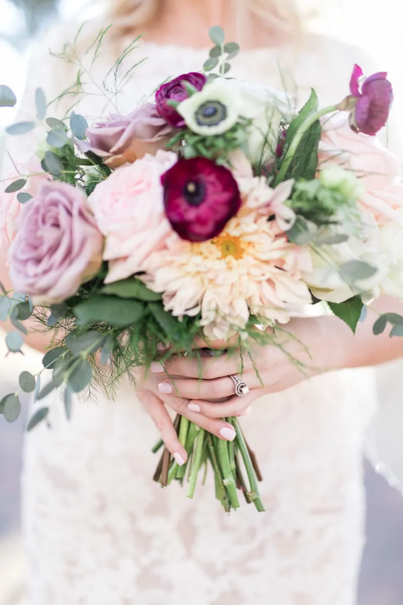 Close view of the burgundy and blush bouquet with the bride's ring hand wrapped around the stems