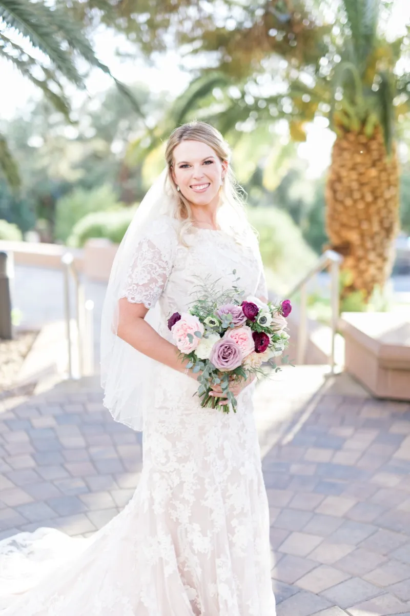 The bride smiling toward the camera with her veil over her shoulders and her bouquet held in front of her