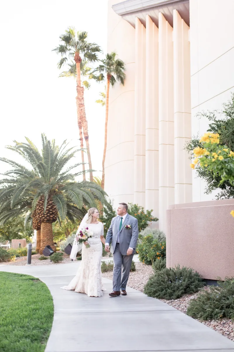 The couple standing on the walkway beside the temple's pale stone wall with palms rising over them