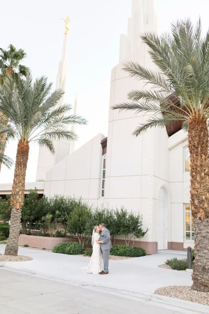 A wide frame of the couple small at the base of the white temple wall between two date palms