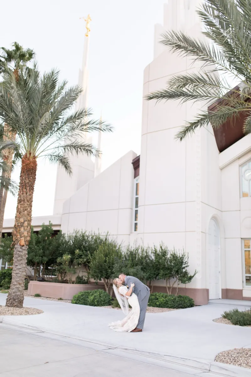 The groom dipping the bride for a kiss with the white temple wall and one of its spires rising behind them