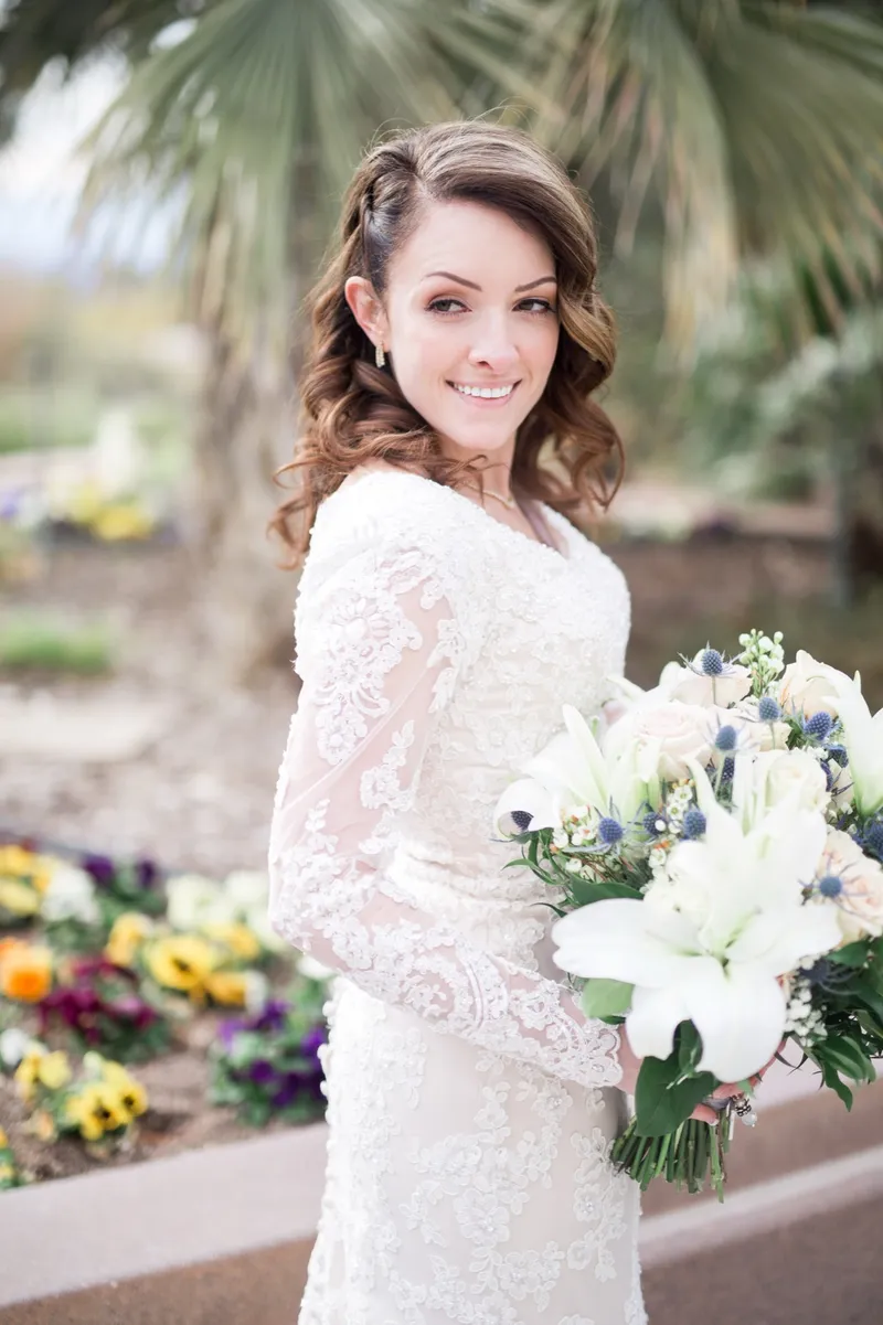 The bride turning toward the camera with a white lily bouquet and a bed of pansies in bloom behind her