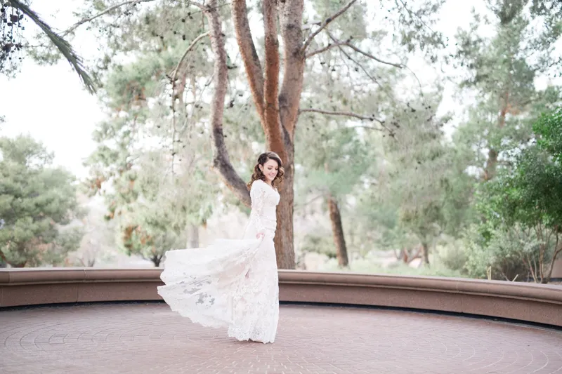 The bride sweeping her lace train around her on the paver plaza with a low curved wall behind her
